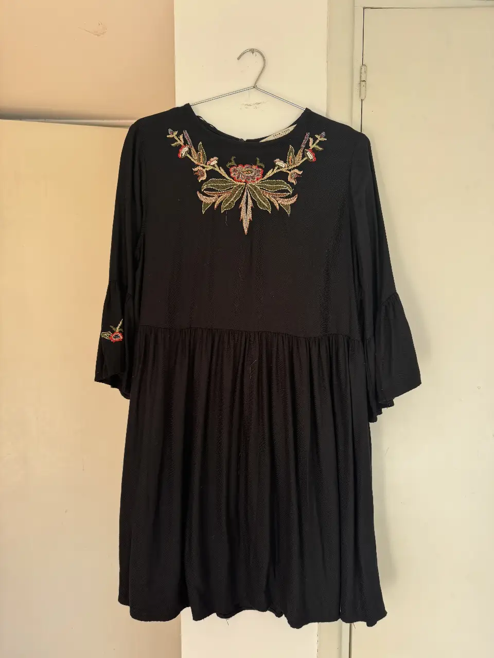 Vestido midi negro con bordado floral en el pecho y mangas acampanadas. Ideal para un look casual con un toque bohemio.