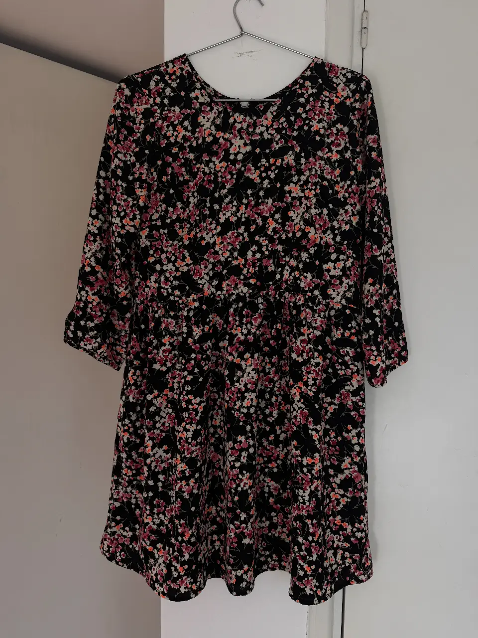 Vestido midi con estampado floral en tonos rosa, blanco y naranja sobre fondo negro. Diseño con mangas 3/4 y cintura marcada. Ideal para un look casual y femenino.