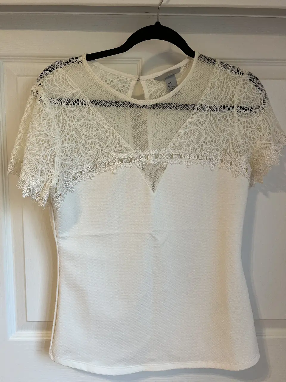 Blusa blanca de encaje con detalles en la parte superior y mangas cortas. Ideal para un look elegante y femenino.