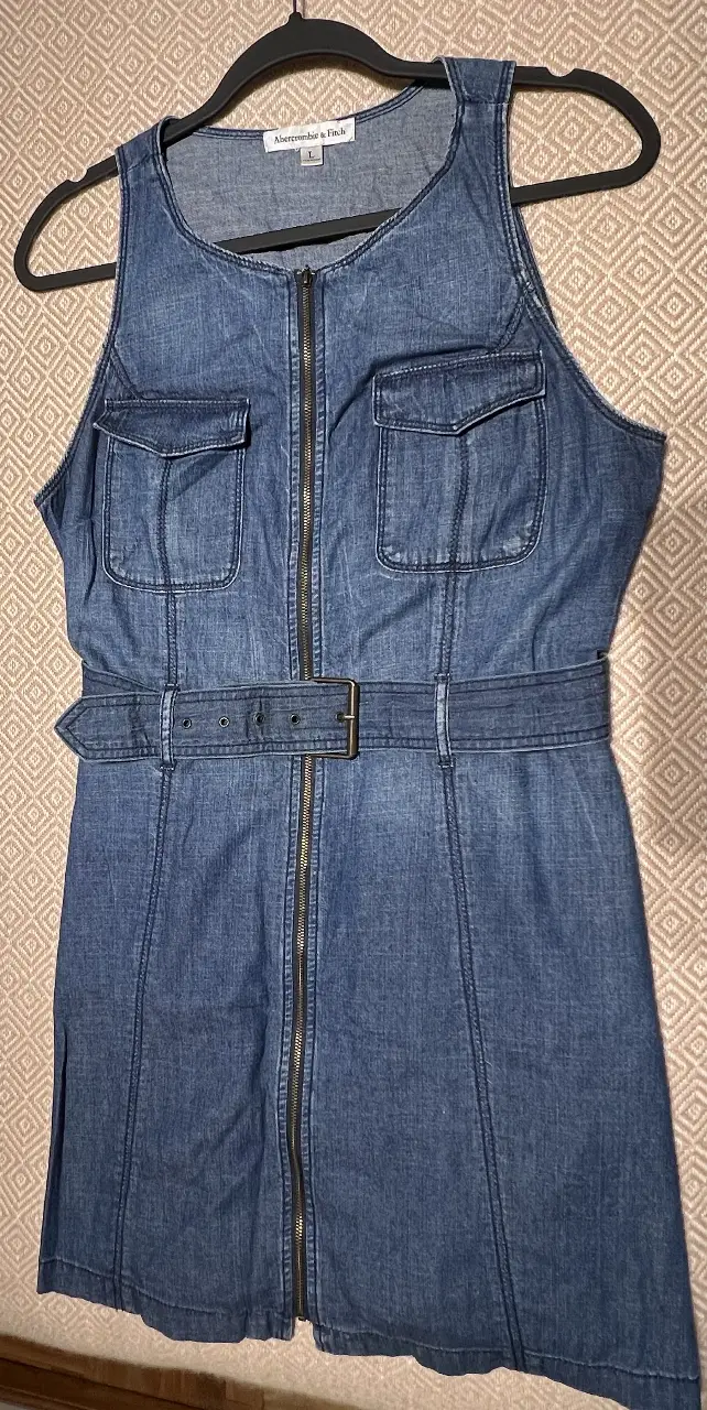 Vestido mini de jean azul, con cierre frontal, bolsillos delanteros y cinturón. Ideal para un look casual y moderno.