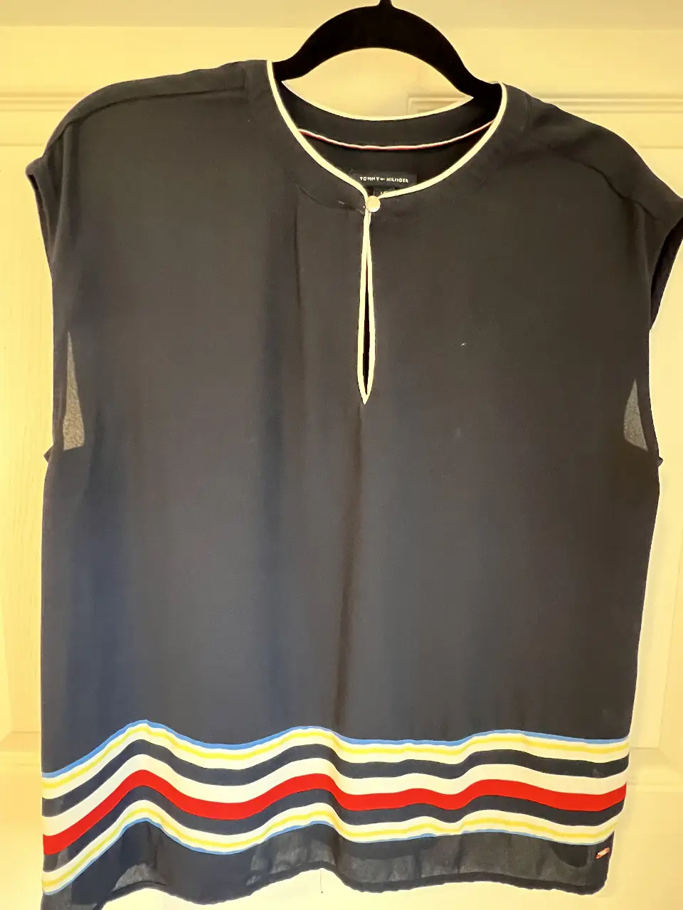 Blusa Tommy Hilfiger azul marino con detalles en blanco y rojo en el bajo. Cuello redondo con detalle de abertura y botón. Ideal para un look casual y elegante.