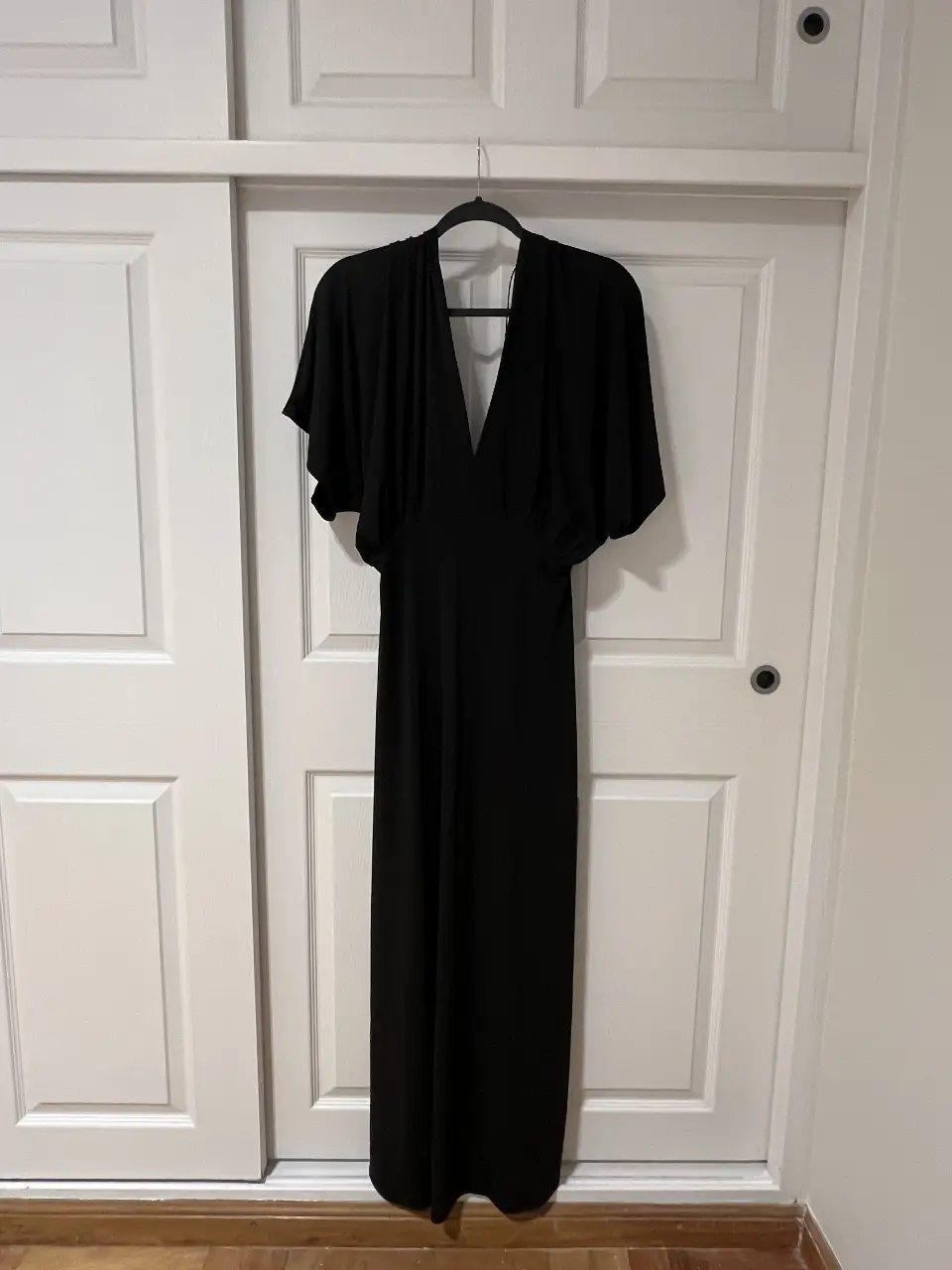 Vestido largo negro con escote en V y mangas cortas tipo capa. Ideal para eventos formales o fiestas. Confeccionado en poliéster y spandex, ofrece comodidad y estilo.