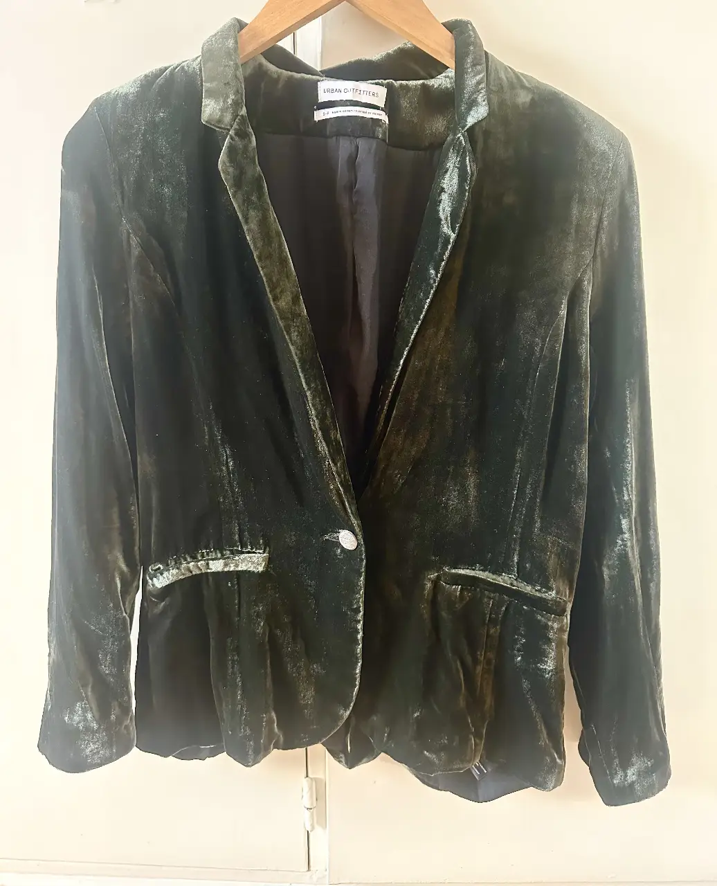 Blazer de terciopelo verde oscuro de Urban Outfitters, con un solo botón y bolsillos delanteros. Ideal para un look elegante y sofisticado.