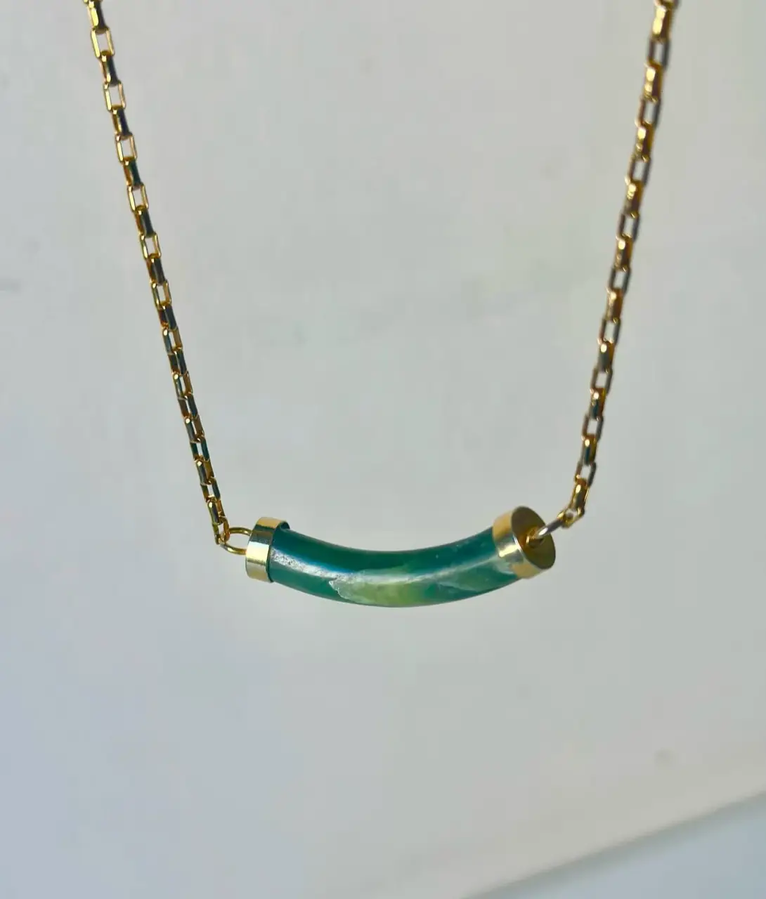 Collar dorado con dije cilíndrico verde. Un accesorio elegante y moderno para cualquier ocasión. Es de Yael G.