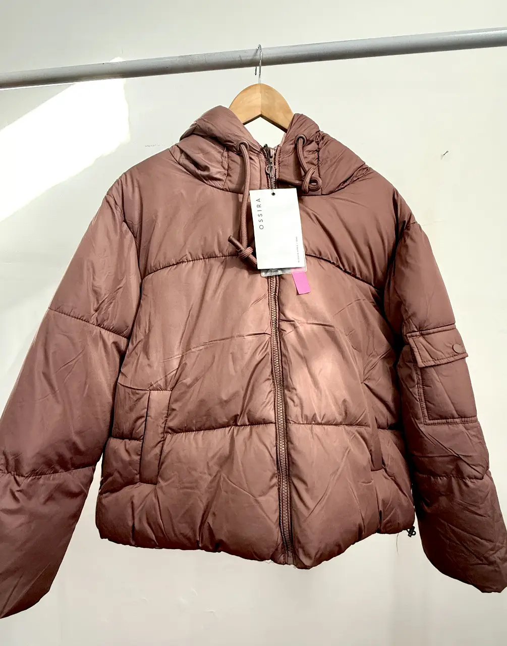 Campera puffer marrón con capucha, ideal para el invierno. Cuenta con cierre frontal, bolsillos y etiqueta de la marca OSSIRA.