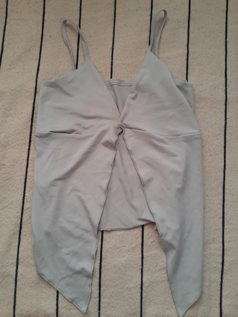 Top gris clarito con tiras finas y escote en V cruzado. Posee un detalle de nudo en el frente y dos tiras largas que caen en la parte inferior.