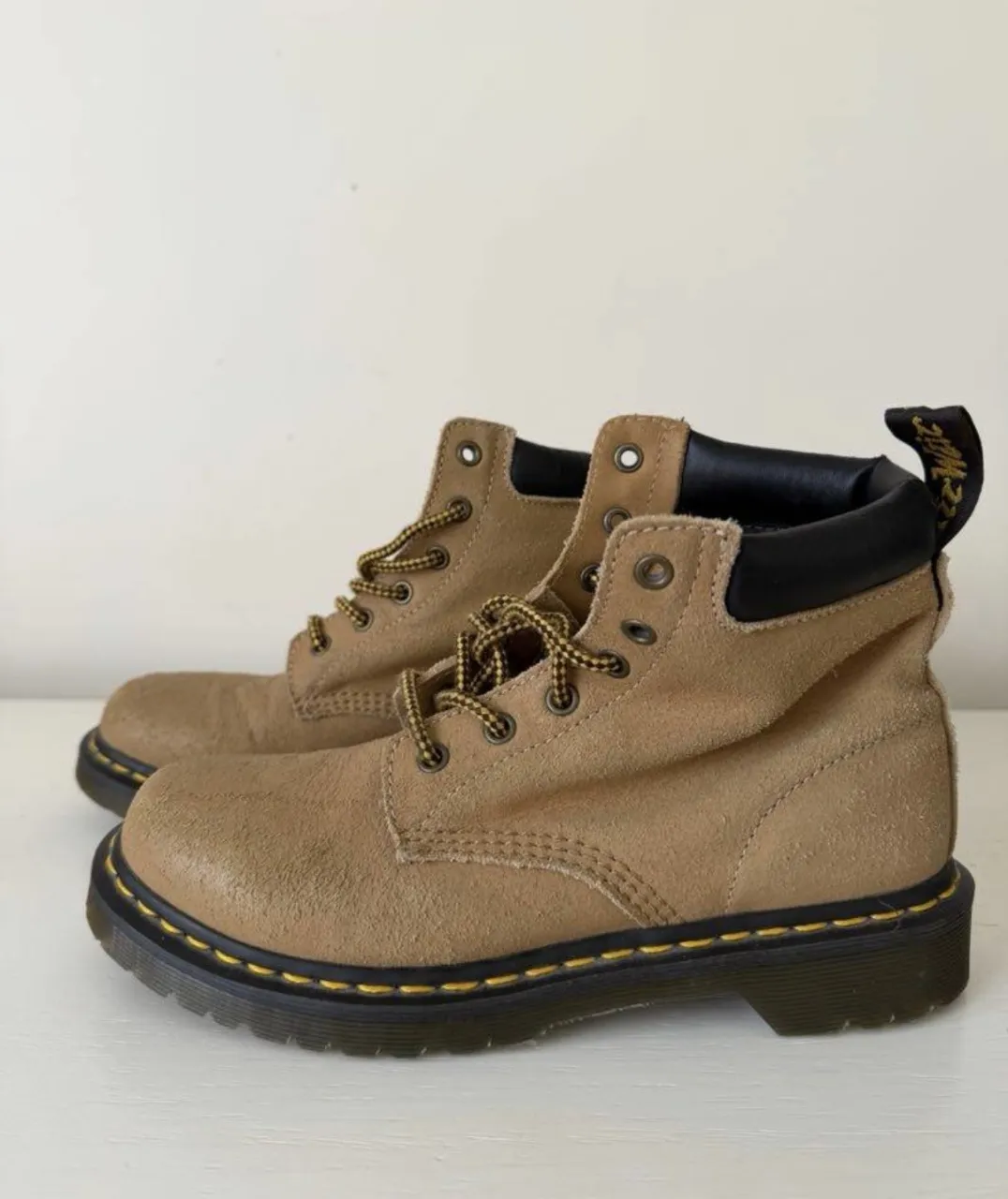 Botas de cuero color suela con cordones amarillos y negros. Detalle de costura amarilla en la suela.