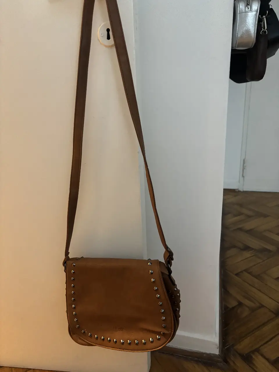 Bandolera marrón de cuero con tachas plateadas, ideal para un look casual y canchero. Marca Prüne.