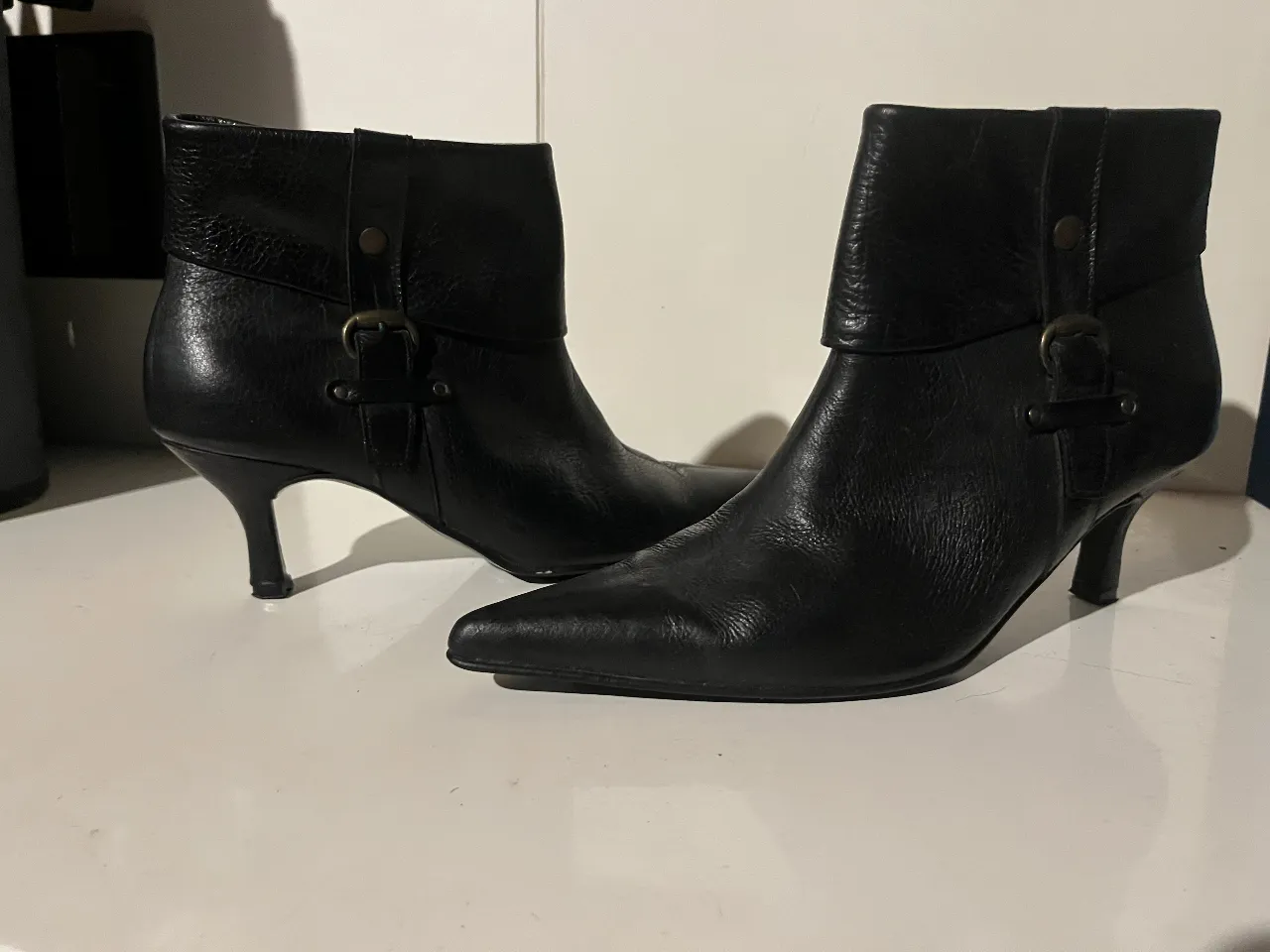 Botines de cuero negro con taco fino y punta. Diseño elegante con detalles de hebilla y cierre lateral. Ideales para un look sofisticado.