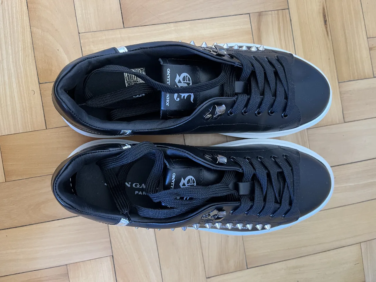 Zapatillas negras de cuero con detalles plateados y tachas. Diseño moderno y elegante, ideales para un look casual con un toque de estilo.