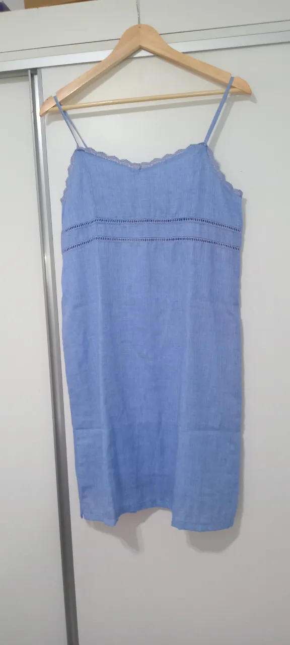 Vestido camisero de lino azul claro con tirantes finos y detalles de encaje en el escote. Posee un corte recto y es ideal para un look fresco y casual.