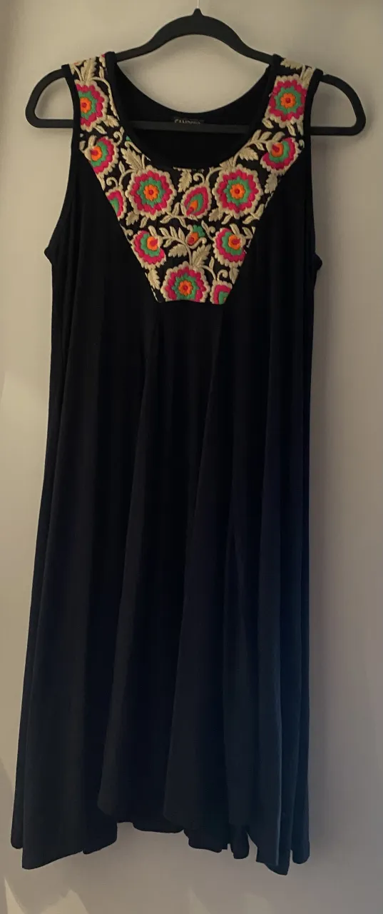 Vestido negro sin mangas con un hermoso bordado floral multicolor en el escote. Ideal para un look fresco y vibrante.