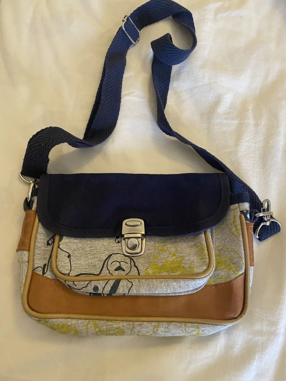 Cartera bandolera con estampa de perritos y detalles en cuero. Ideal para el día a día, con un diseño divertido y práctico. Cierre metálico y correa ajustable.