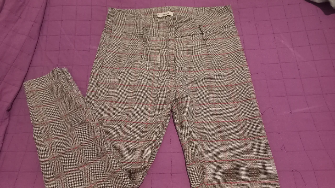 Pantalón sastrero de mujer, con estampado a cuadros en tonos grises y detalles en rojo. Tiro alto y corte recto, ideal para un look elegante y moderno.