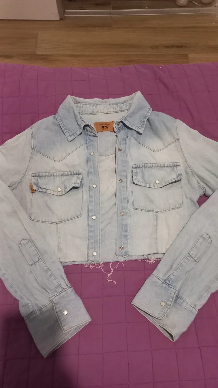 Campera de jean cropped celeste claro con detalles desgastados. Posee dos bolsillos delanteros con solapa y botones metálicos. Ideal para un look casual y moderno.