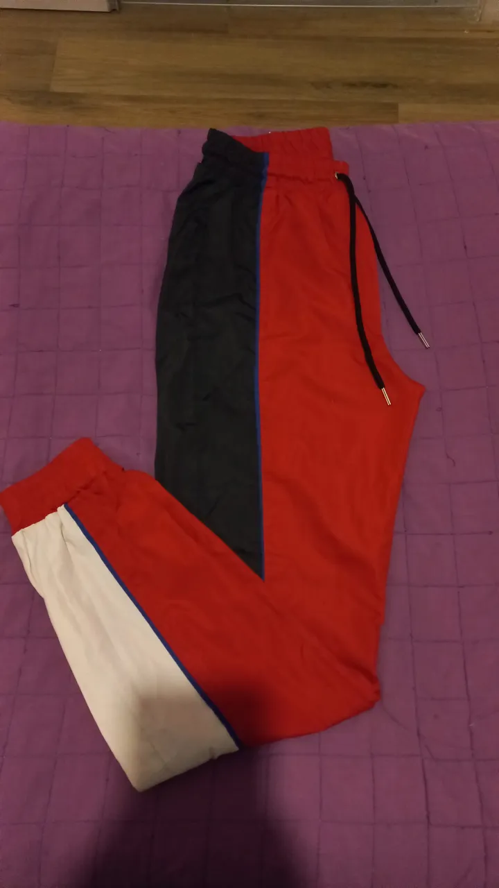 Pantalón deportivo para mujer, con diseño bicolor en rojo y negro. Posee detalles en blanco y azul, y un cordón ajustable en la cintura. Ideal para un look casual y cómodo.