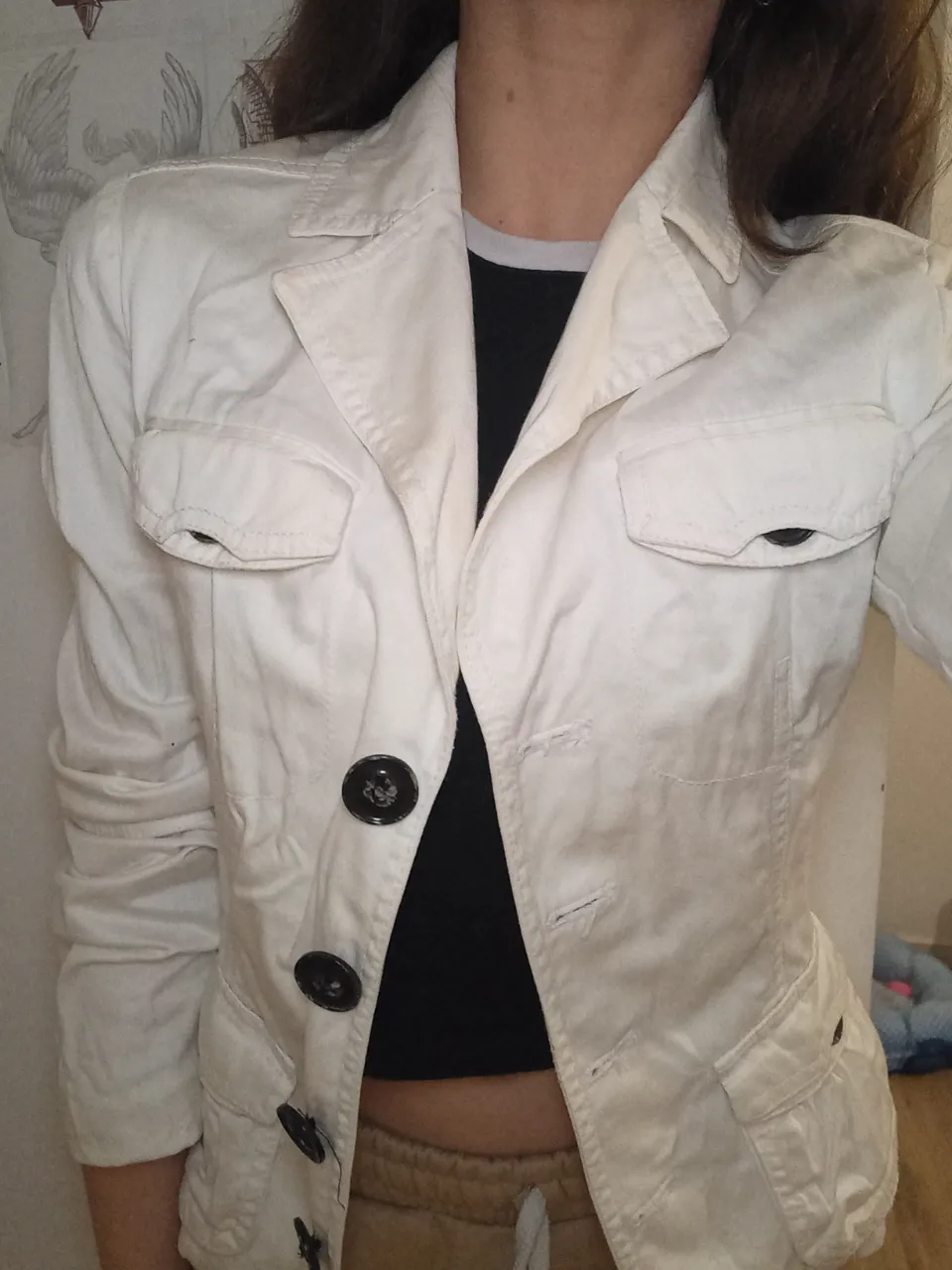 Chaqueta blazer blanca de mujer, con dos bolsillos delanteros y botones negros. Ideal para un look elegante y versátil.