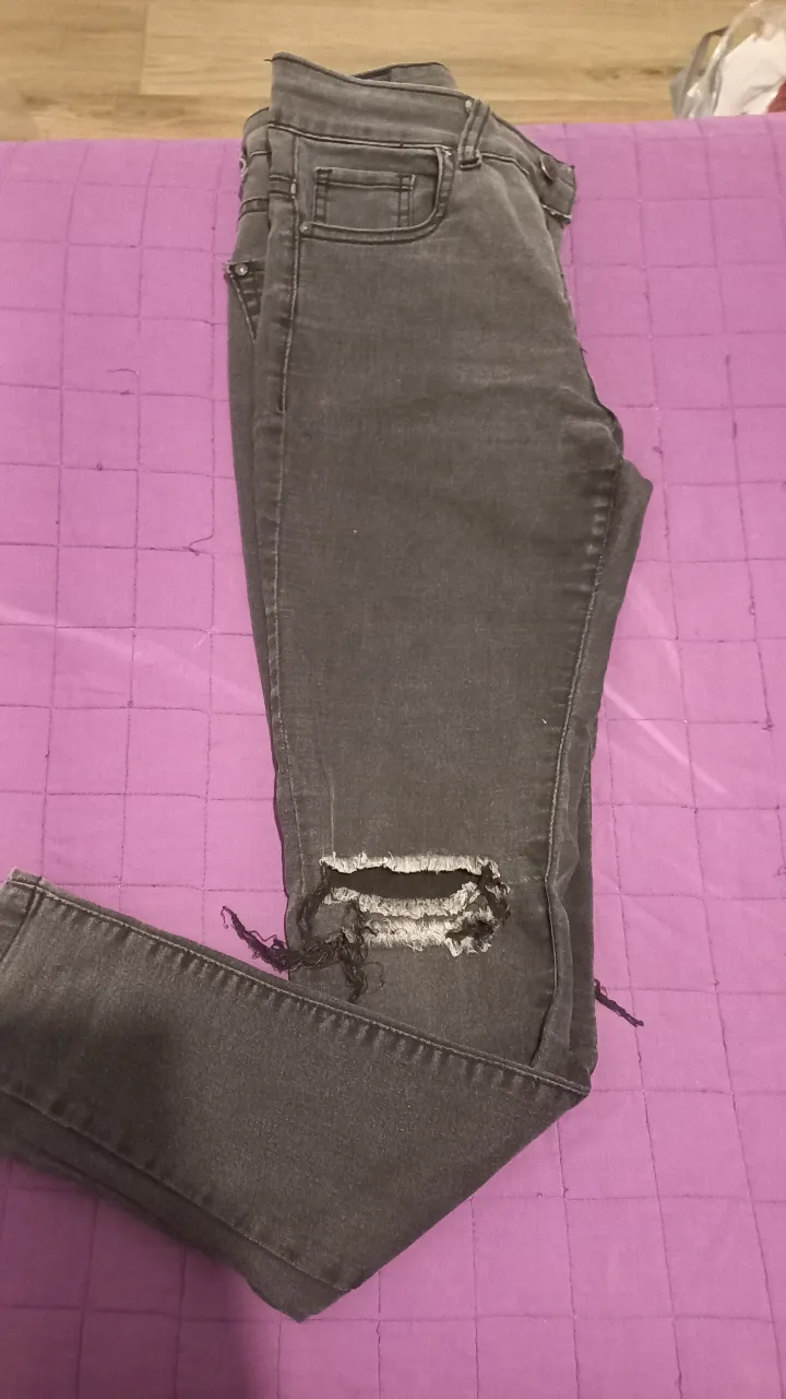 Jeans de mujer grises con roturas en la rodilla. Tiro medio, corte skinny. Ideal para un look casual y moderno.