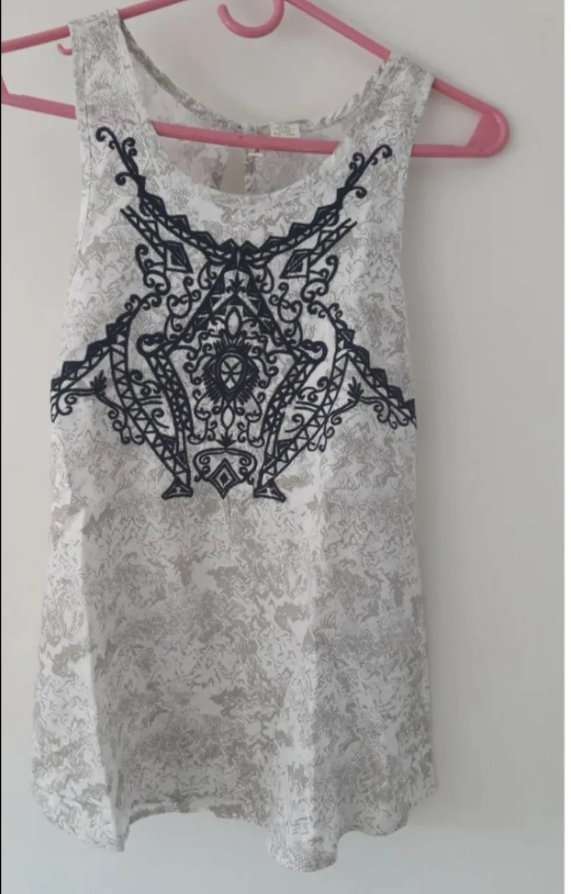 Musculosa blanca con estampado abstracto en tonos grises y un delicado bordado negro en el frente. Ideal para un look casual y fresco.
