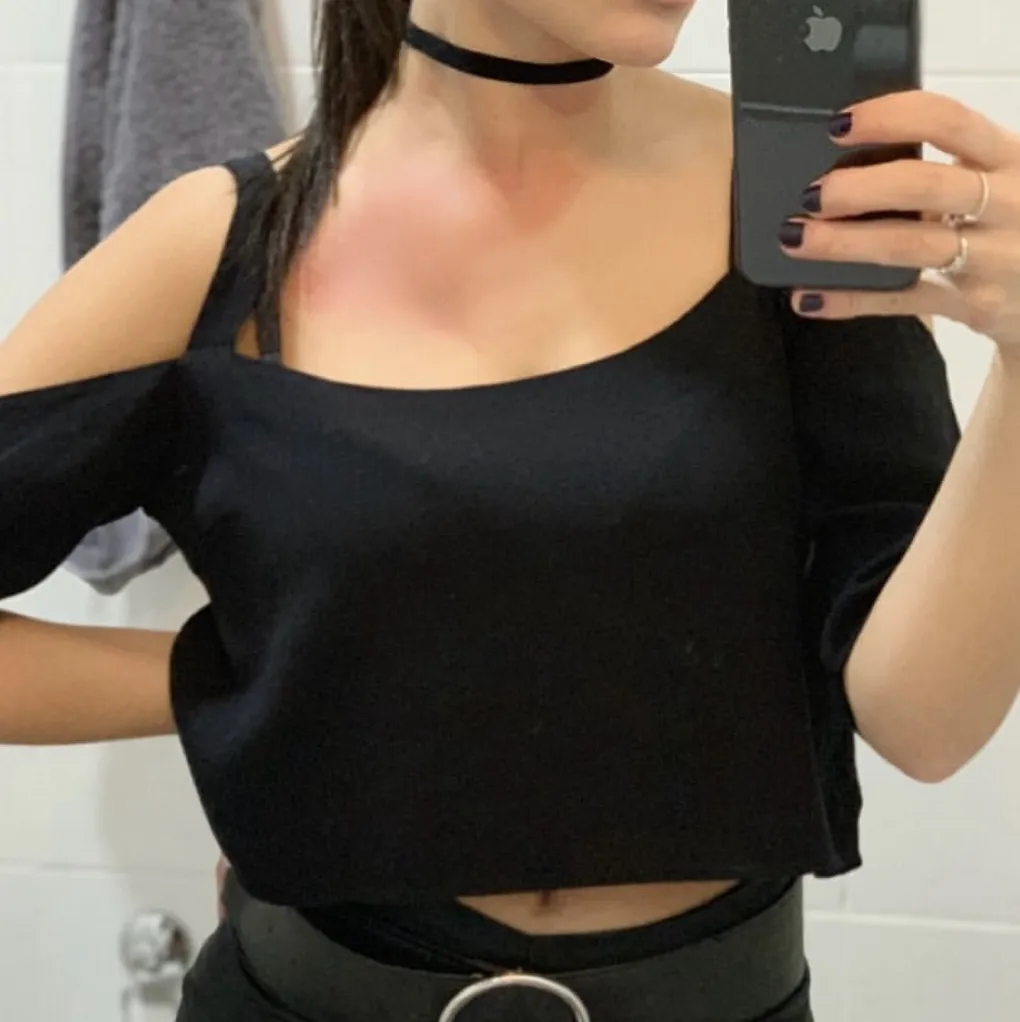 Remera negra corta con mangas caídas y escote cuadrado. Detalle de tiras en los hombros.