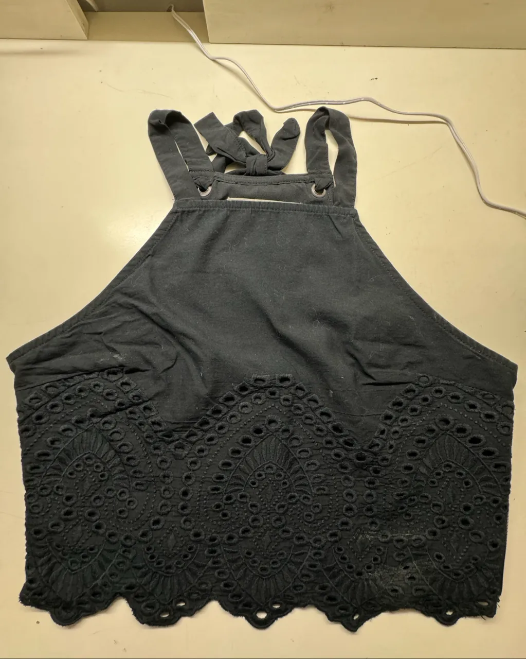 Top negro con tiras anudadas en la espalda y detalle de bordado calado en la parte inferior. Posee cierre lateral.