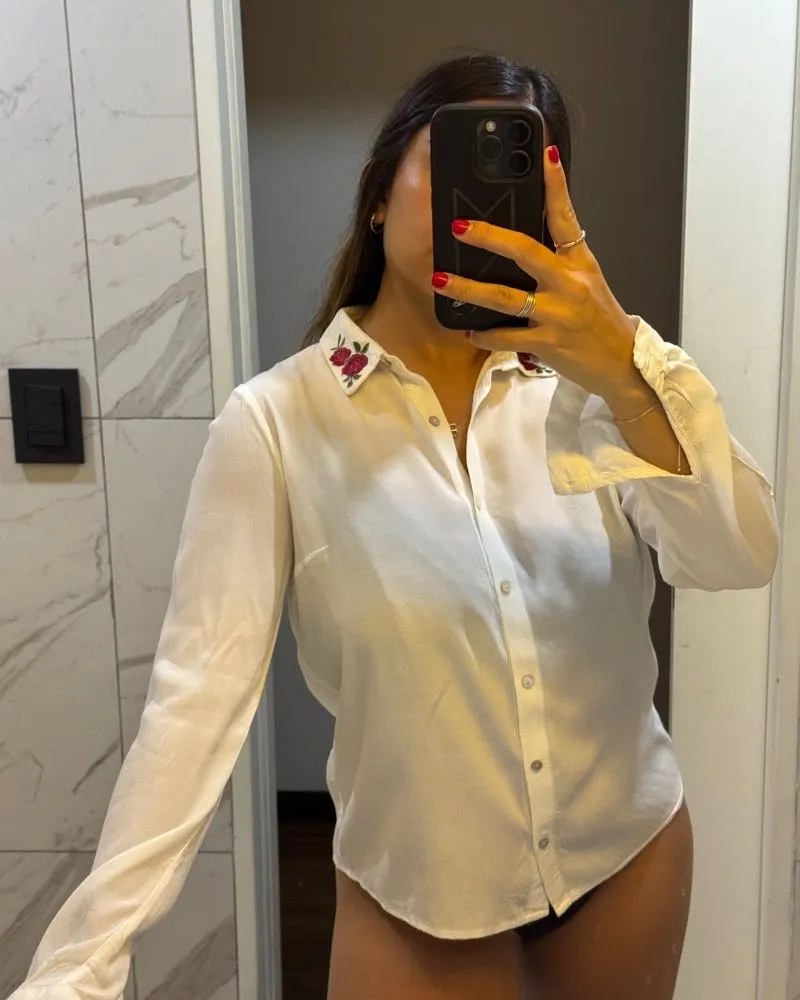 Camisa blanca de manga larga con un delicado bordado de flores rojas en el cuello. Un toque romántico y chic para cualquier ocasión.