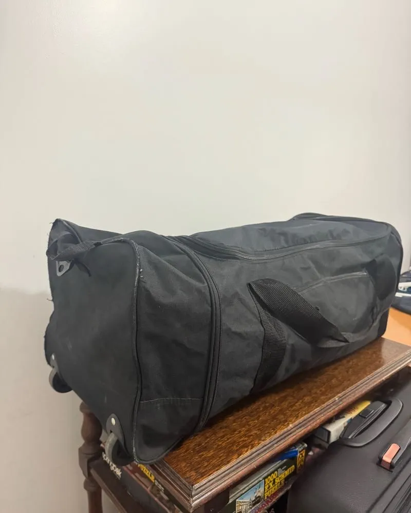 Bolsón de viaje negro con ruedas, ideal para escapadas o viajes largos. Amplio espacio interior y compartimentos para organizar tus pertenencias. Resistente y práctico.