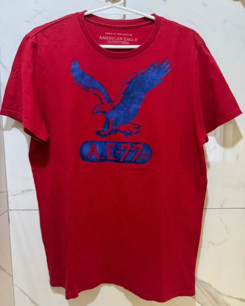 Remera roja de manga corta con estampa de águila y "AE 77" en azul. Ideal para un look casual y relajado.