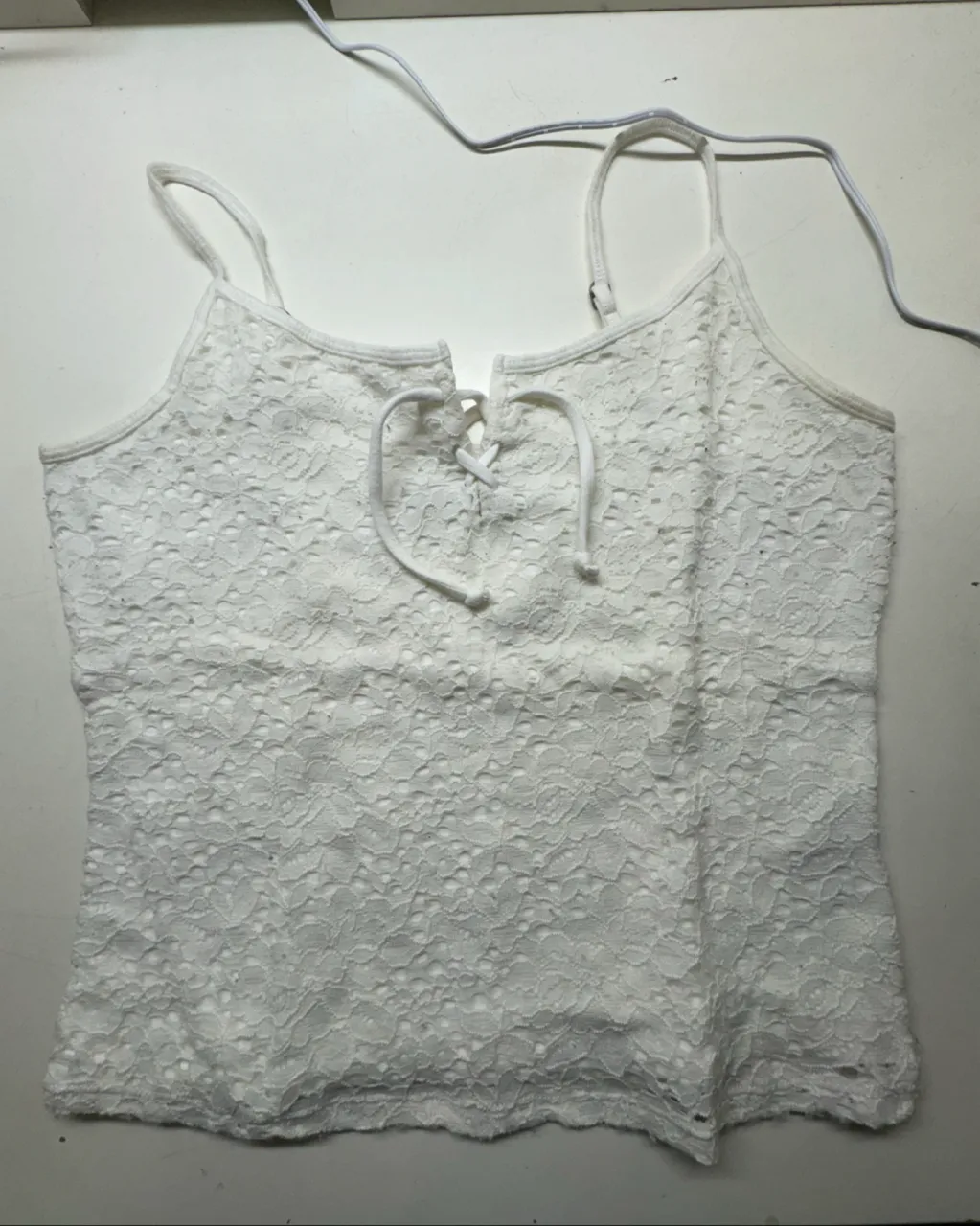 Top blanco de encaje con tiras finas y detalle de lazo en el escote.