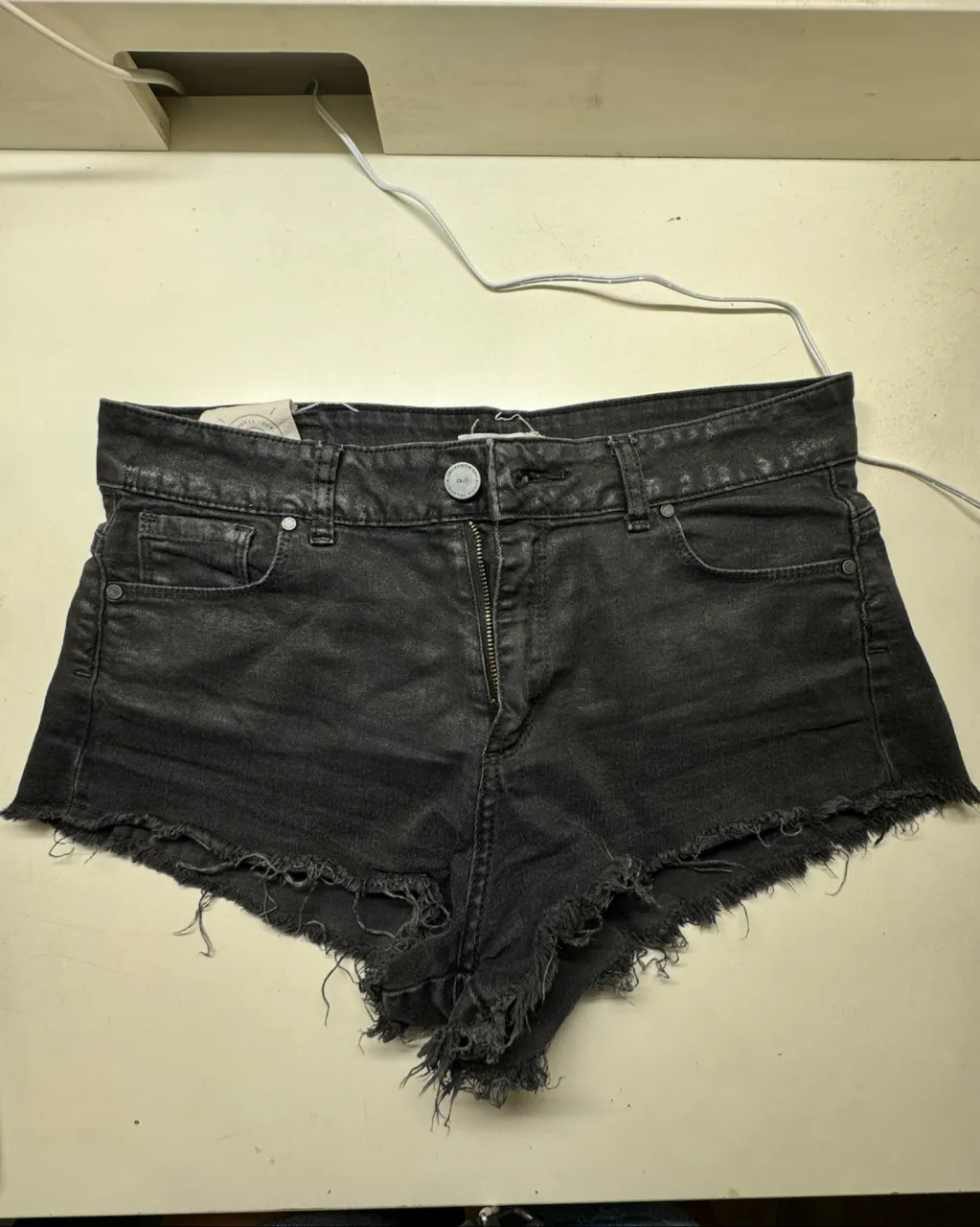 Shorts de jean negros con roturas y flecos en el ruedo. Cierre con botón y cierre.