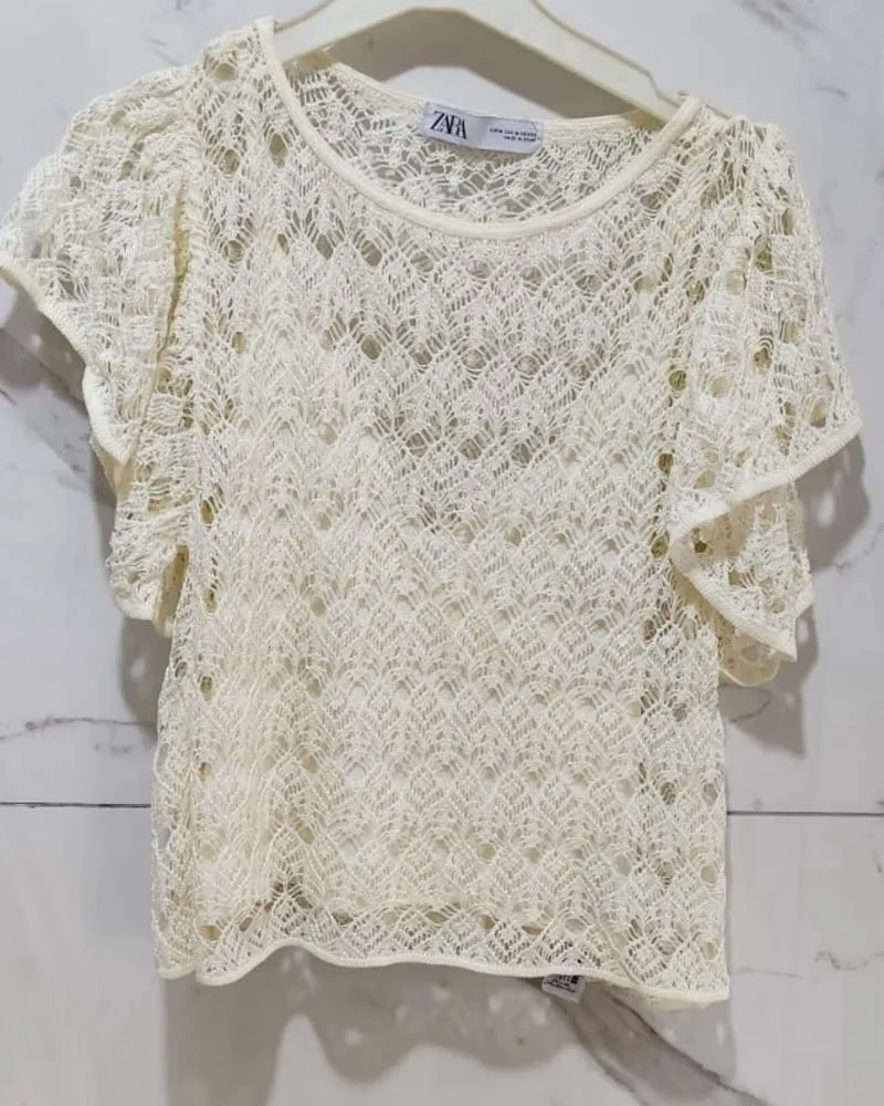 Remera de tejido de crochet color crudo con mangas cortas y cuello redondo.