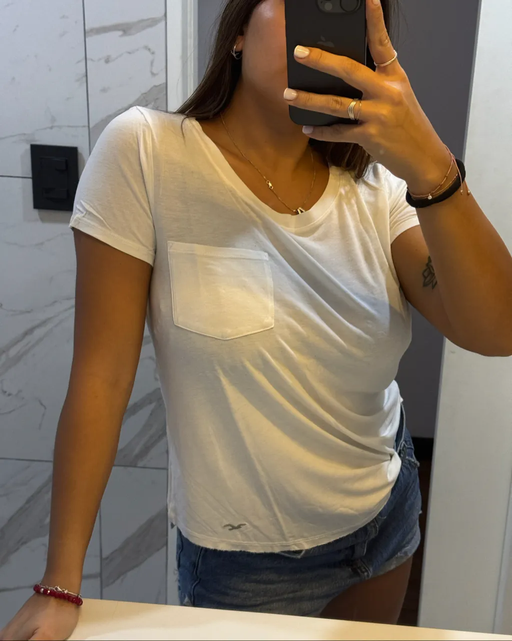 Remera blanca de manga corta con bolsillo en el frente. Posee un pequeño logo de un ave en la parte inferior izquierda.