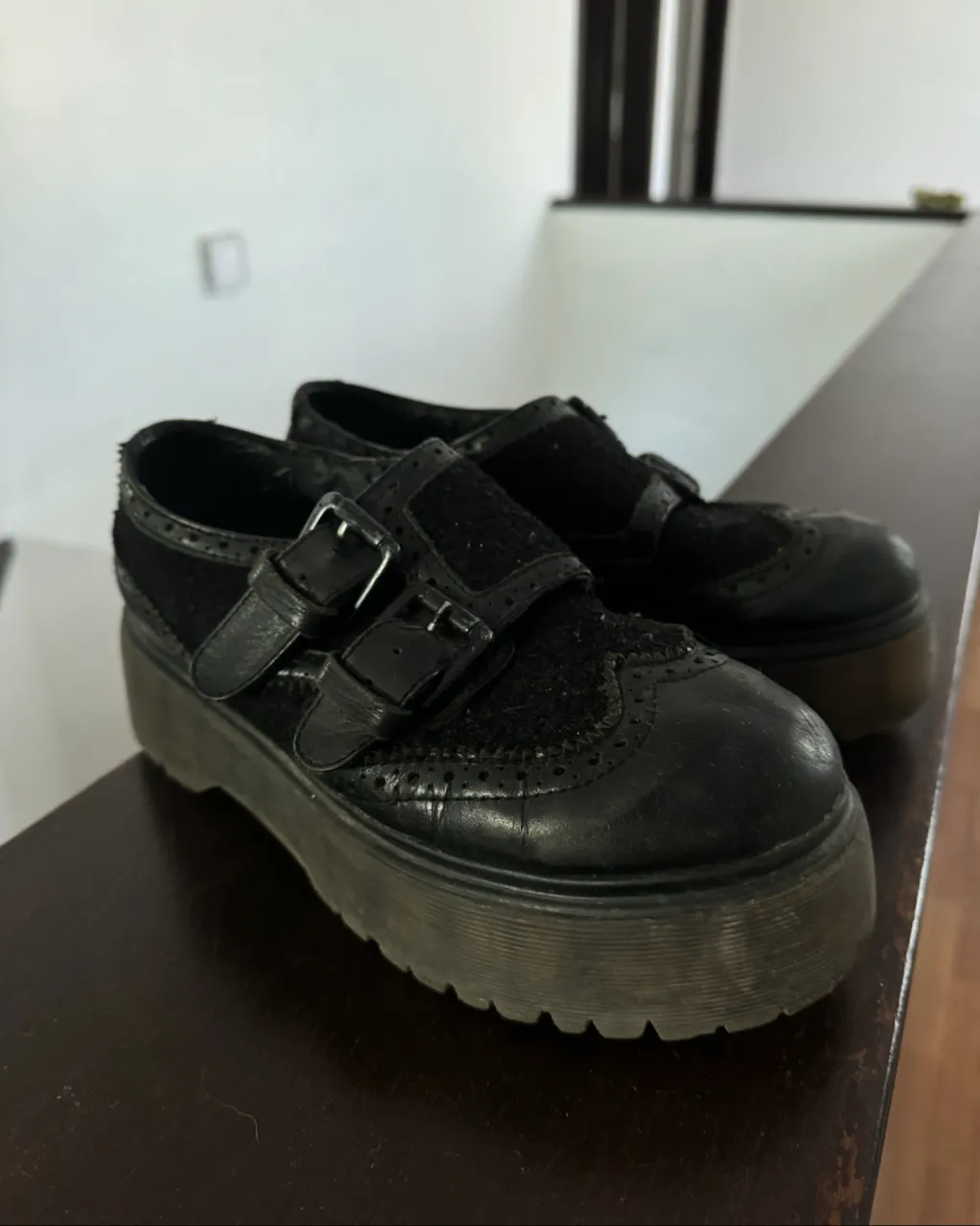Zapatos negros de plataforma con doble hebilla y detalles de perforaciones.