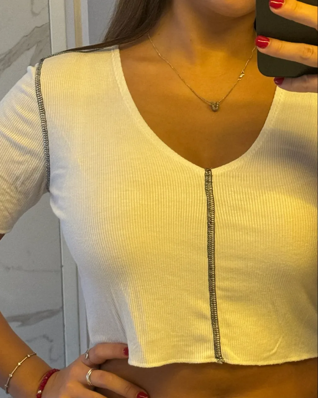 Remera blanca de manga corta con costuras grises a la vista. Posee un escote en V con una costura central que se extiende hasta el borde inferior.