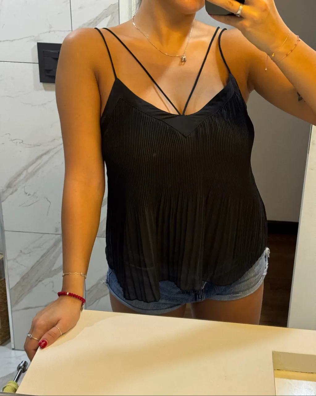 Top negro de breteles finos con escote en V y detalles de frunces verticales. La parte superior del escote tiene un detalle de tela en forma de V.