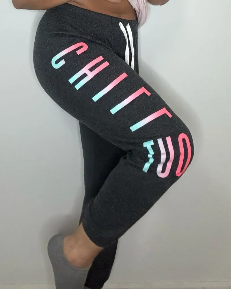 Pantalon de frisa gris oscuro con estampa lateral de letras en degradé rosa y celeste. Cintura con cordón blanco. Ideal para un look comfy y relajado.