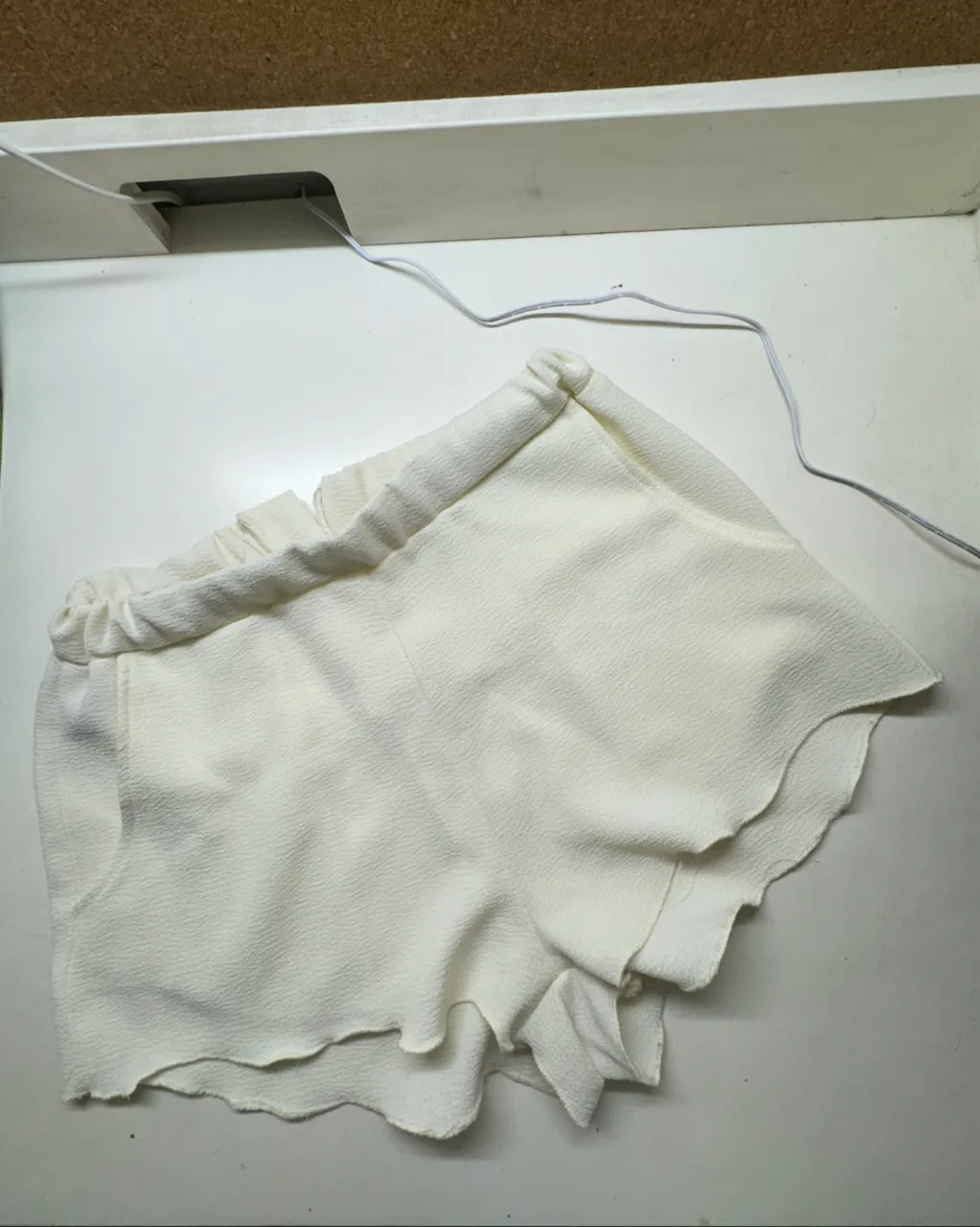 Shorts blancos con cintura elastizada y detalle de volados en la parte inferior. Poseen bolsillos laterales y cierre metálico en uno de los laterales.