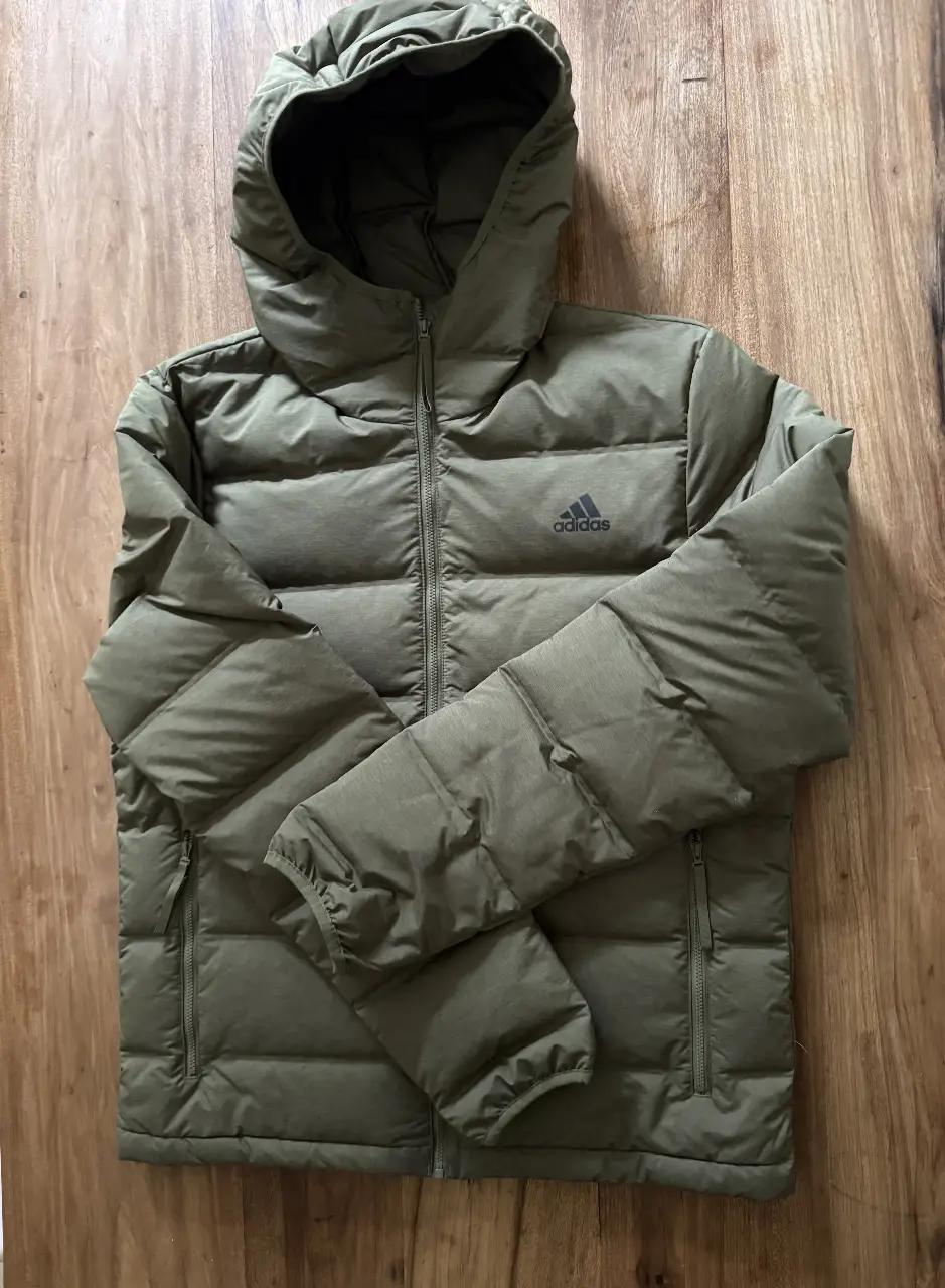 Campera Adidas acolchada con capucha, color verde oscuro, con cierre frontal y logo de la marca. Ideal para el invierno.