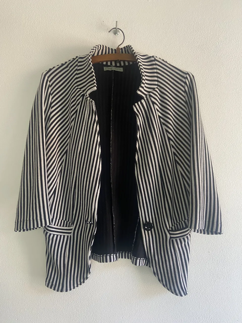 Blazer a rayas verticales blancas y negras. Tiene un solo botón al frente y bolsillos con solapa.