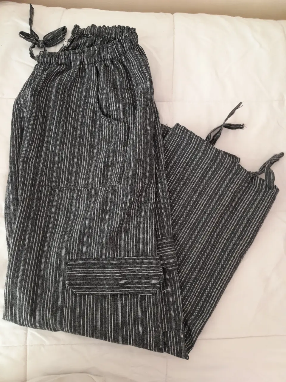 Pantalón suelto de tela rayada en gris y blanco, con bolsillos y detalles de ajuste en los tobillos. Ideal para un look casual y cómodo.