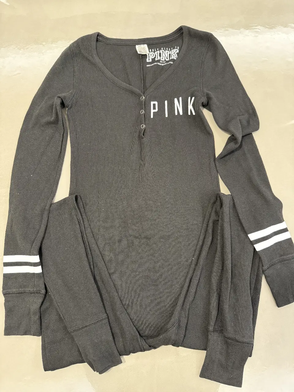 Enterito de pijama negro de la marca PINK, con detalles en blanco. Tiene mangas largas y un corte cómodo. Ideal para estar en casa.