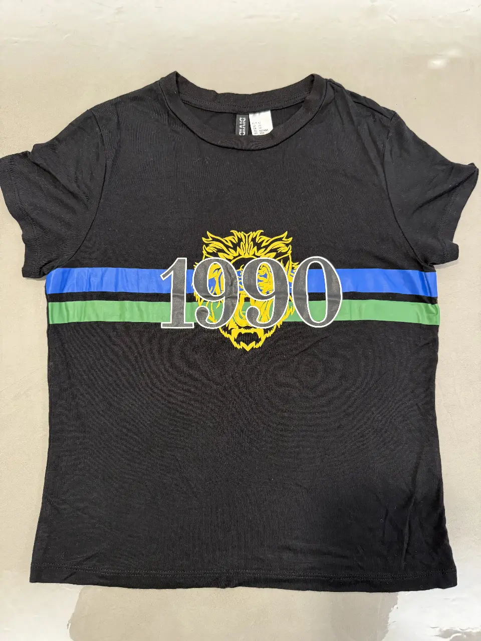 Remera negra de hombre de la marca H&M, con diseño estampado "1990" en el frente. Posee una franja horizontal azul y verde. Talle XS.