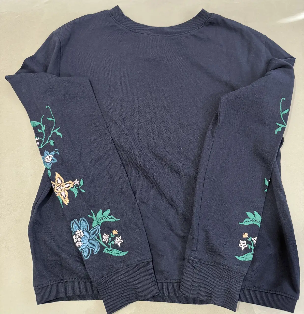 Buzo de cuello redondo azul marino con bordado floral en las mangas. Ideal para un look casual y cómodo.