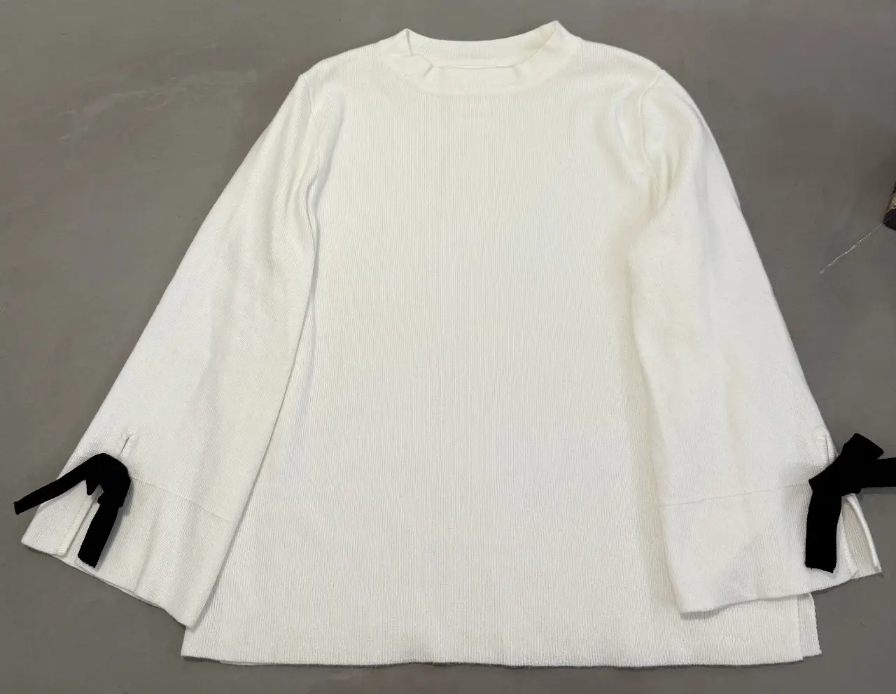 Sweater de niña blanco con mangas acampanadas y detalles de lazo negro en los puños. Ideal para un look elegante y abrigado.