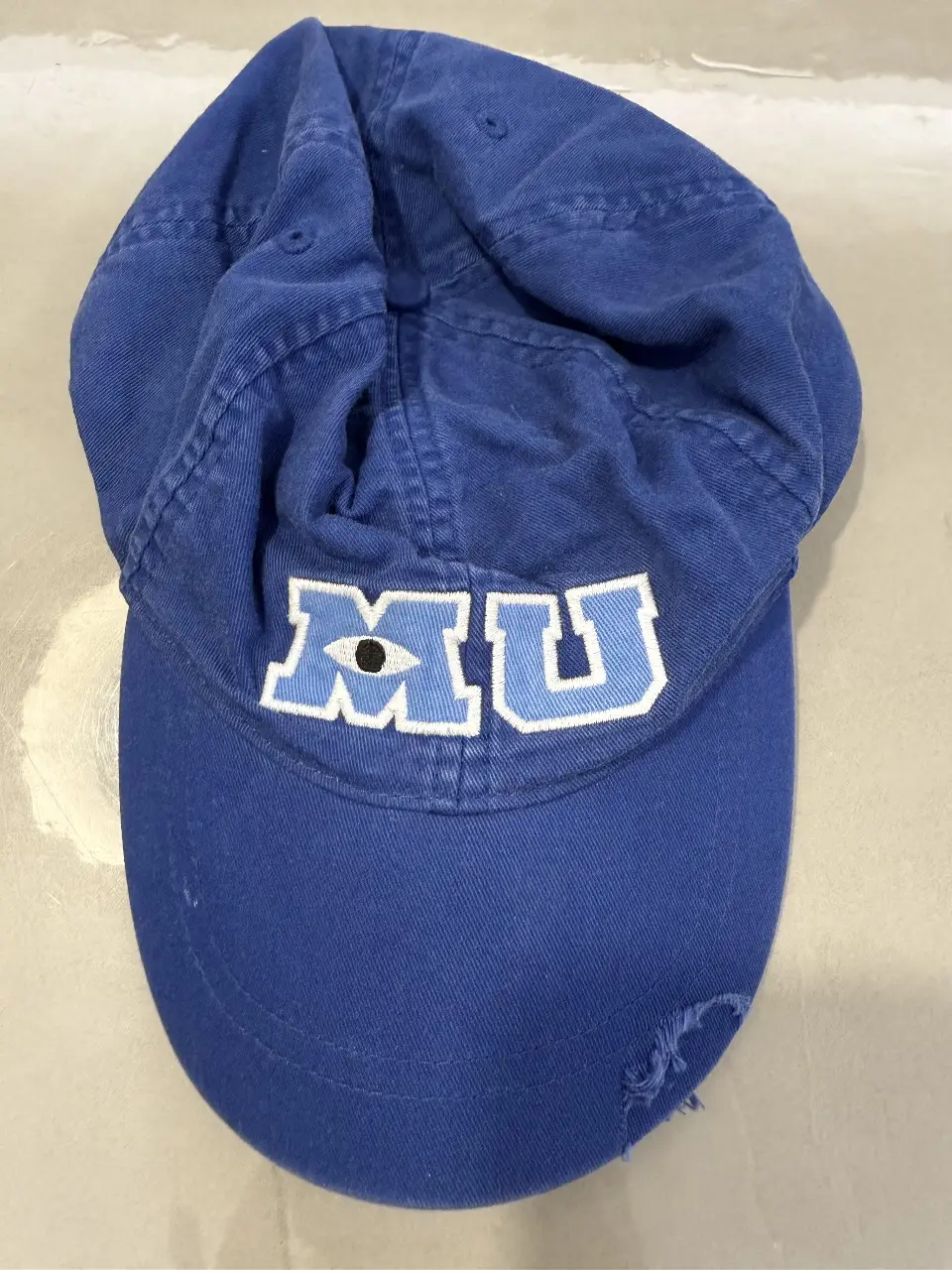 Gorra azul de Monsters University con el logo MU bordado. Ideal para fanáticos de Disney y para un look casual y deportivo.