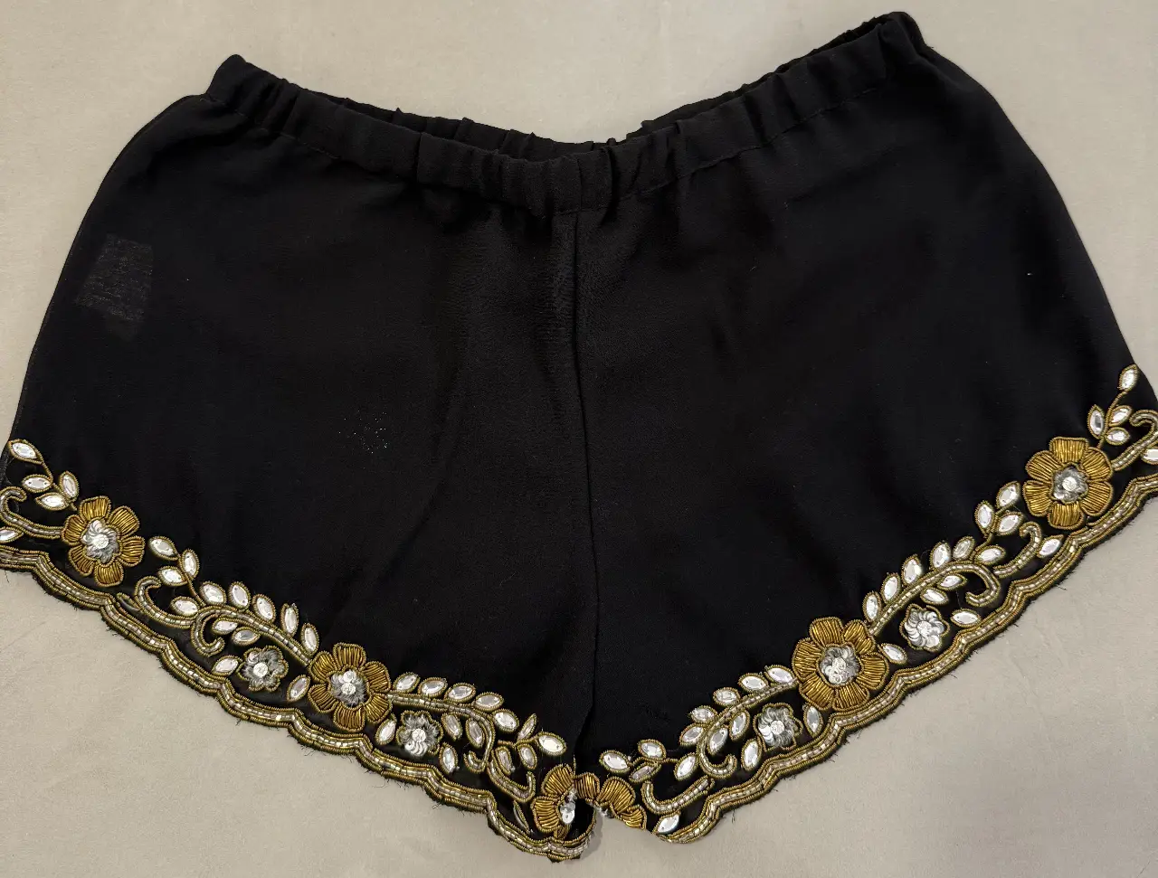 Shorts negros de tela con detalles dorados y pedrería en el borde inferior. Ideal para fiestas o salidas.