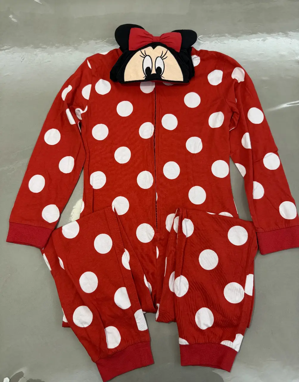 Pijama entero de Minnie Mouse para niña, con diseño de lunares rojos y blancos. Incluye capucha con la cara de Minnie. Ideal para estar cómoda y abrigada en casa.