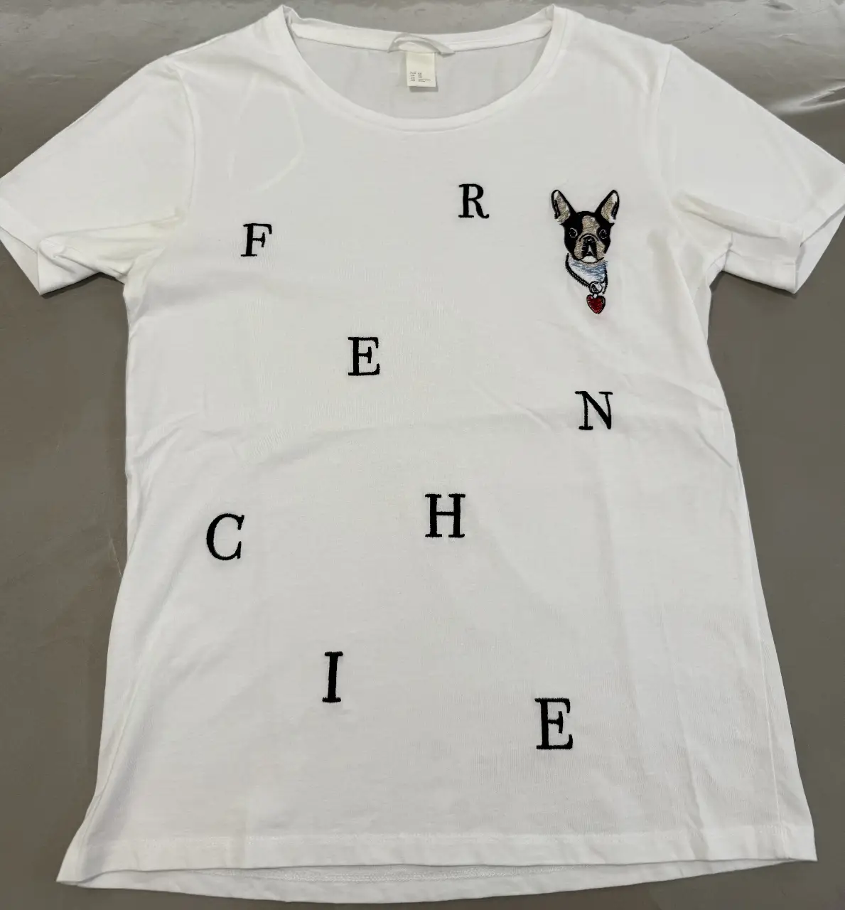 Remera blanca de algodón con estampado de un bulldog francés y letras bordadas. Ideal para un look casual y canchero.