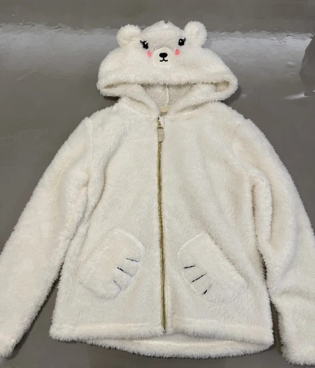 Buzo con capucha de oso polar para niña, con cierre frontal dorado y bolsillos delanteros. Detalles de orejas y cara de oso en la capucha. Ideal para el invierno.