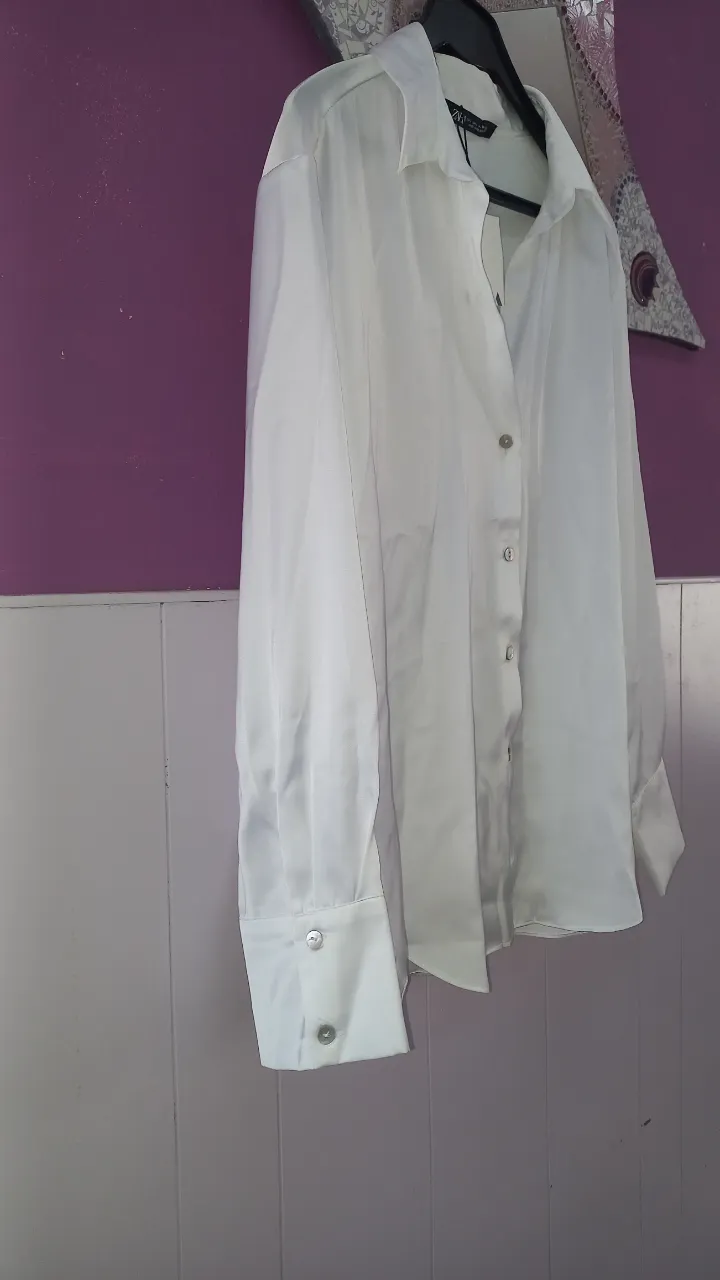 Camisa blanca de manga larga con botones al frente y puños anchos con botones.